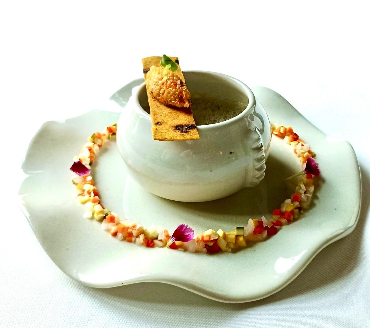 Soup in a white pot with a ring of diced vegetables
